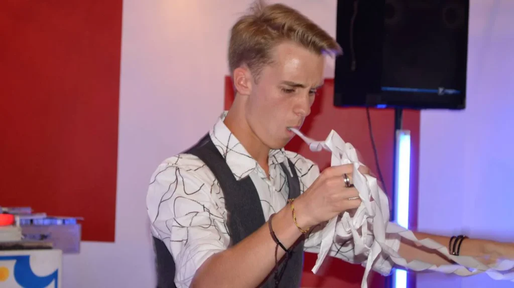 eligius jeune qui fais un tour de magie en sortant un corde en papier qui sort de sa bouche sans s'arrêter